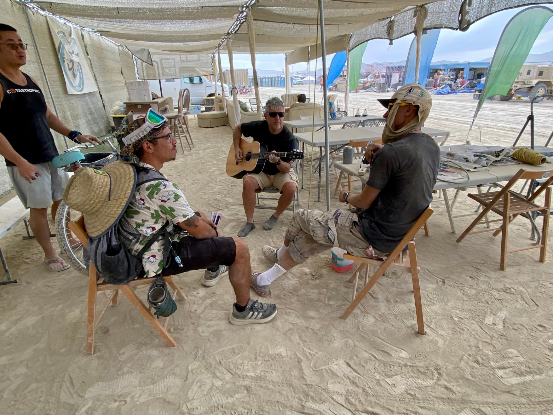 Campers relaxing and playing guitar under the shade structure