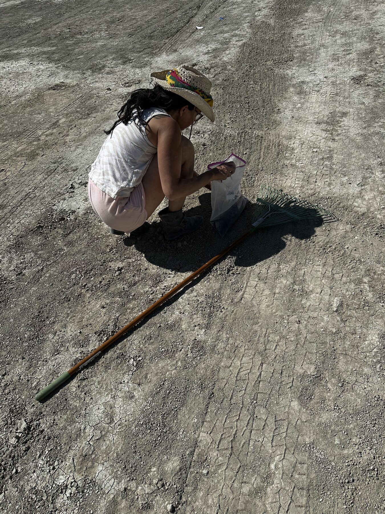 A camper bagging collected MOOP next to a rake on the open playa