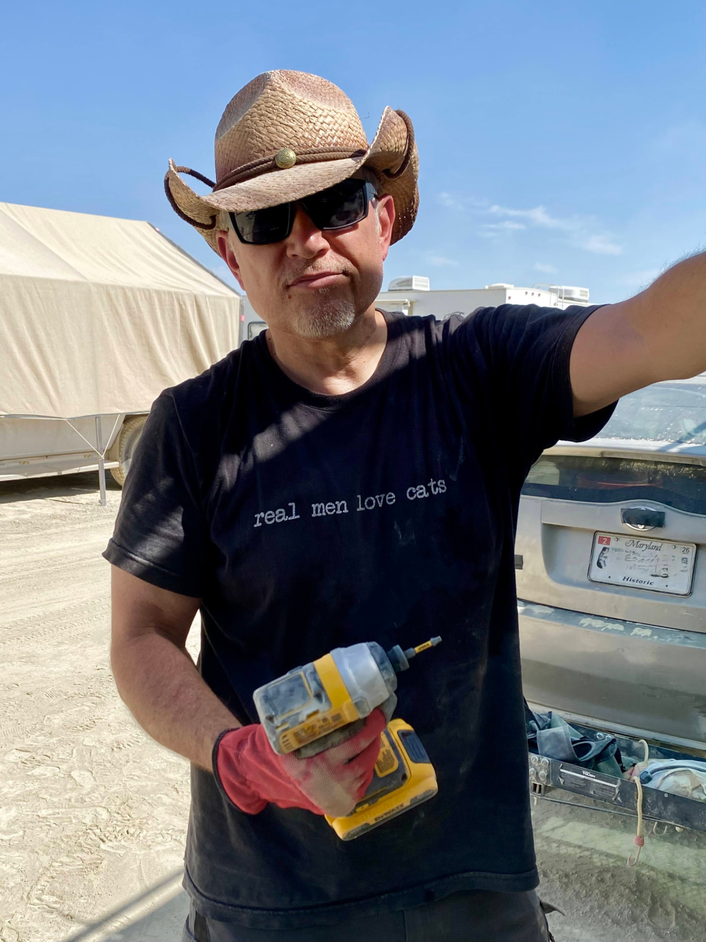 A camper in a cowboy hat holding a power drill at the build site