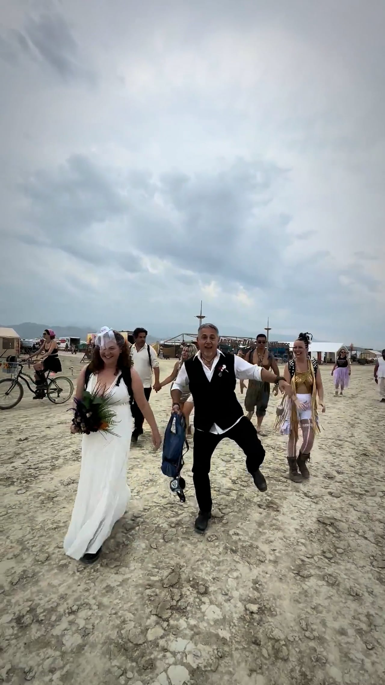 Two couples married on playa, surrounded by Vivarium campers, 2025