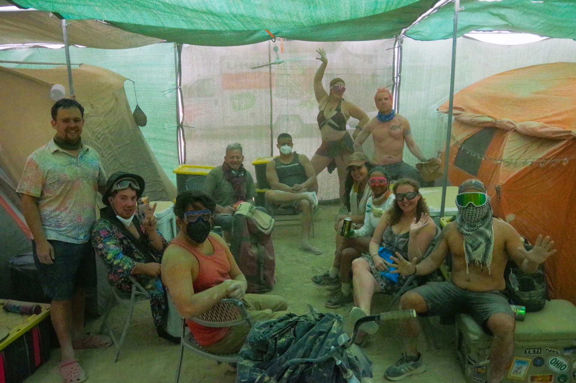 A group of campers in goggles under green shade cloth during a storm